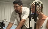 Still from the Channel 13 News feature: Daniel Yamin beside a participant wearing an EEG electrode cap